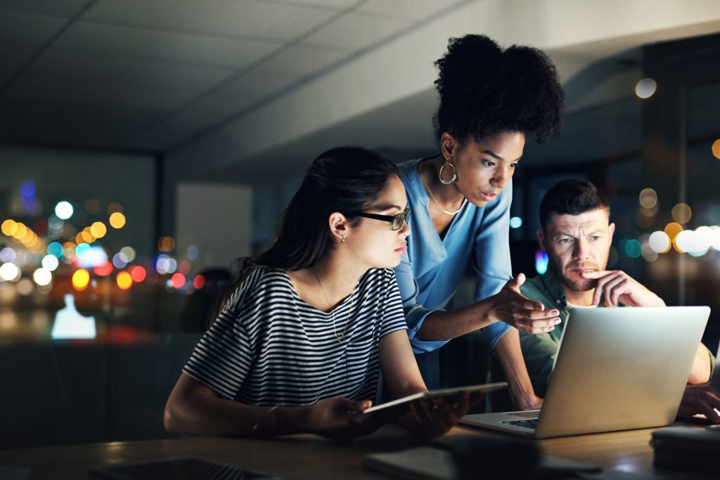 Three people looking at laptop screen at night