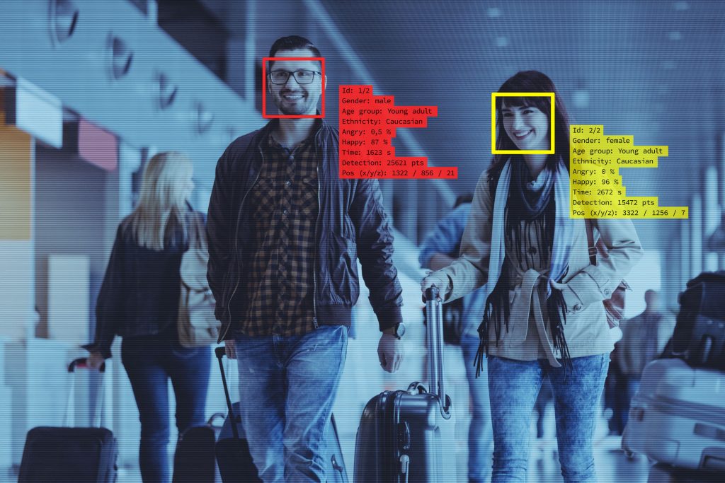 Two people walking through an airport on security screen with their details displayed beside them