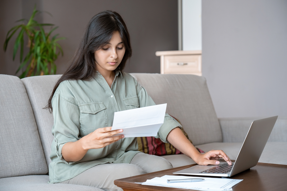 Young Indian woman looking at letter while using laptop