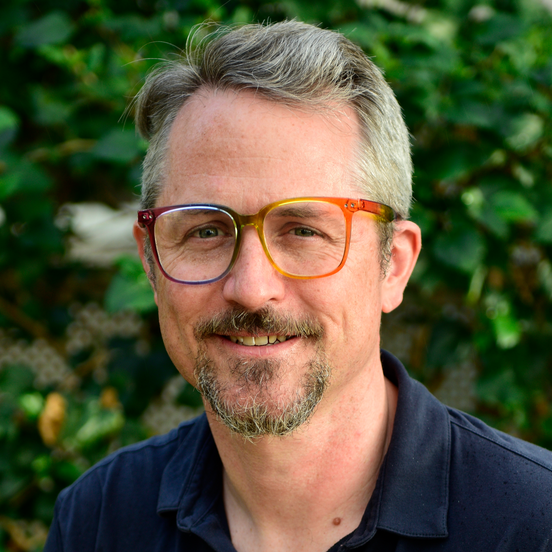 Sam_Gregory Photo of Sam Gregory. Sam has salt and pepper hair, a goatee and brightly coloured glasses. He wears a dark blue, collared shirt.