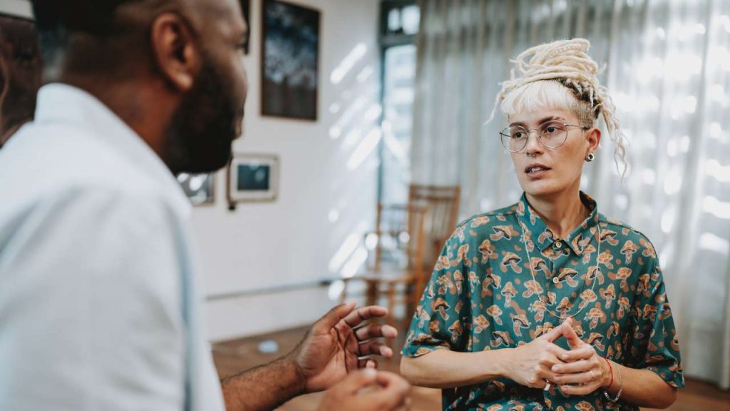 Two people in a room facing each other talking in therapy session.