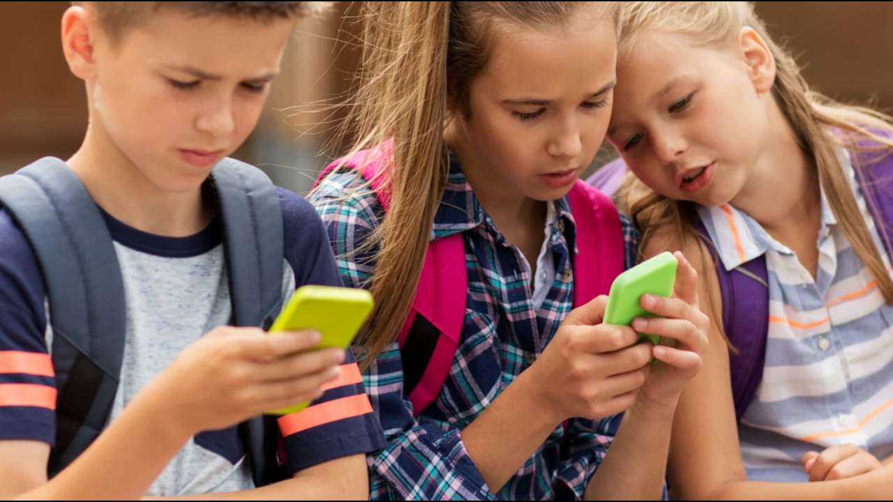 Three young children looking at mobile phones.